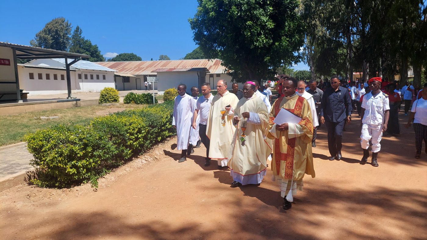 Un corteo di sacerdoti con le vesti bianche e dorate che cammina lungo un viale dell’ospedale