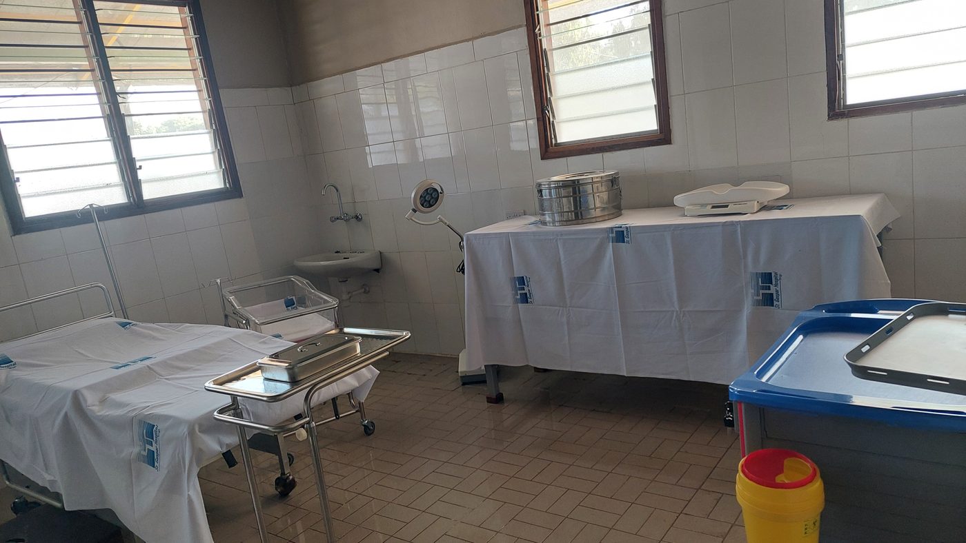 Una sala del reparto con le piastrelle bianche, un lettino coperto da un telo, una culla e un tavolo con gli strumenti